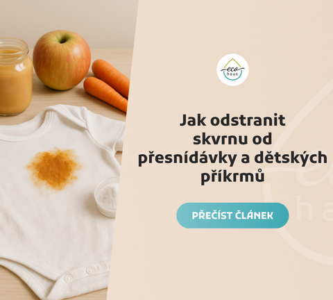 A white baby onesie with a large orange food stain lies on a light wooden surface.
