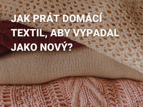 Obrázek s textem 'Jak prát domácí textil, aby vypadal jako nový?' na pozadí složených pletených a tkaných textilií v různých barvách, včetně béžové, červené a růžové. Obrázek má edukativní charakter a poskytuje rady pro správnou péči o domácí textil.